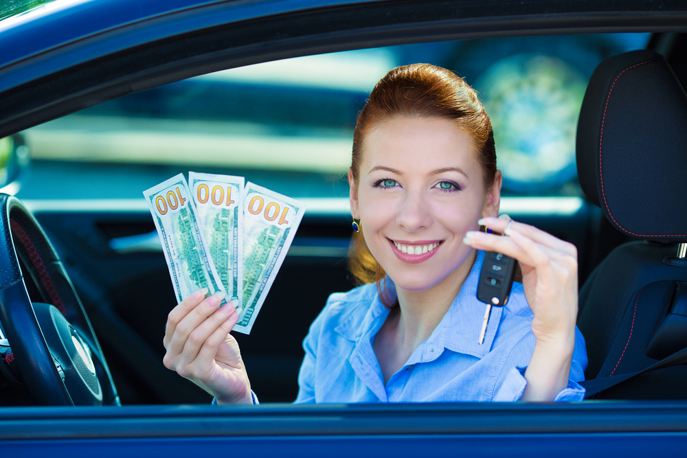 Woman holding car keys and cash inside a vehicle.
