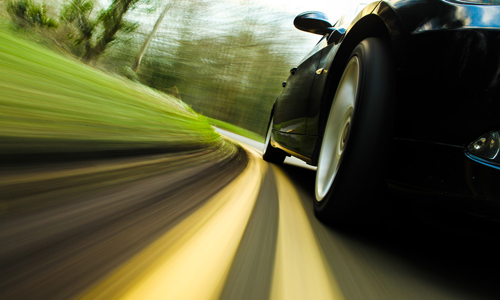 Black car driving on a winding road with motion blur.